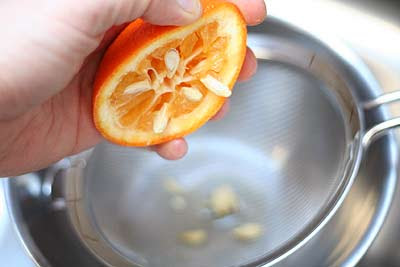 Half an orange with the seeds being removed into a bowl