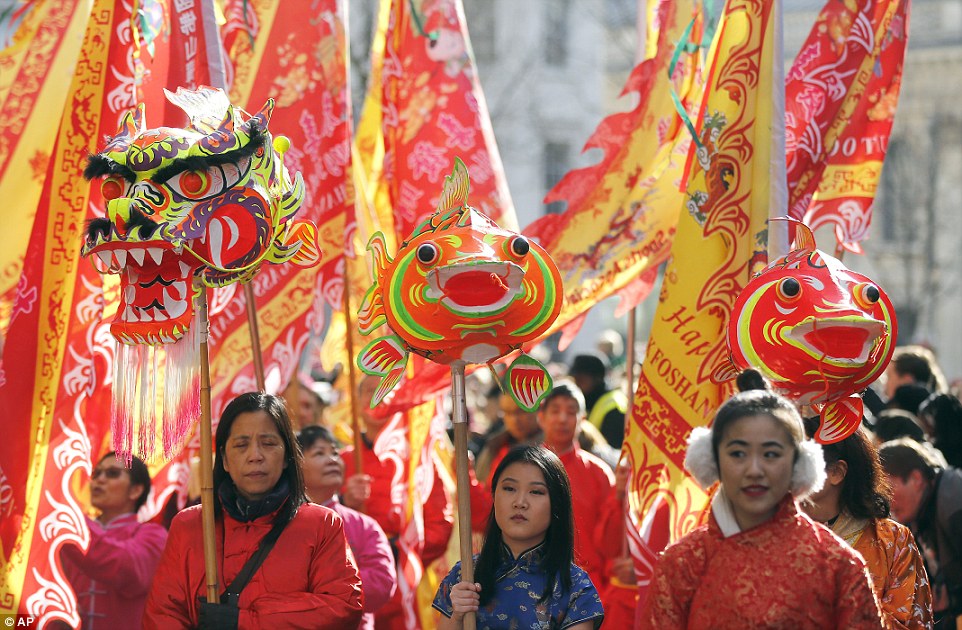 Beautifully adorned flags were carried through London during the  celebration. Some members of the procession held delicately crafted dragon and carp heads suspended on poles. In Chinese mythology, carp are believed to be able to transform into dragons. One woman (centre) can be seen wearing a blue figure-hugging traditional Chinese dress known as a cheongsam, while another festival-goer (right) keeps the cold away with a pair of fluffy white ear muffs